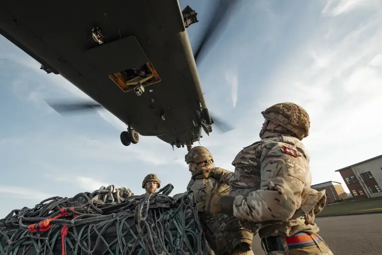 Soldiers wearing their camouflage uniform and helmets stand waiting with a load as a chinook coming into be loaded.