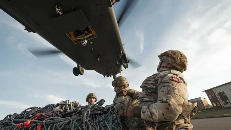 Soldiers wearing their camouflage uniform and helmets stand waiting with a load as a chinook coming into be loaded.