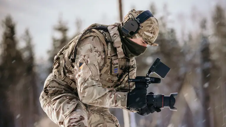 A British Army Photographer holds his camera while he films activity in a snow landscape.