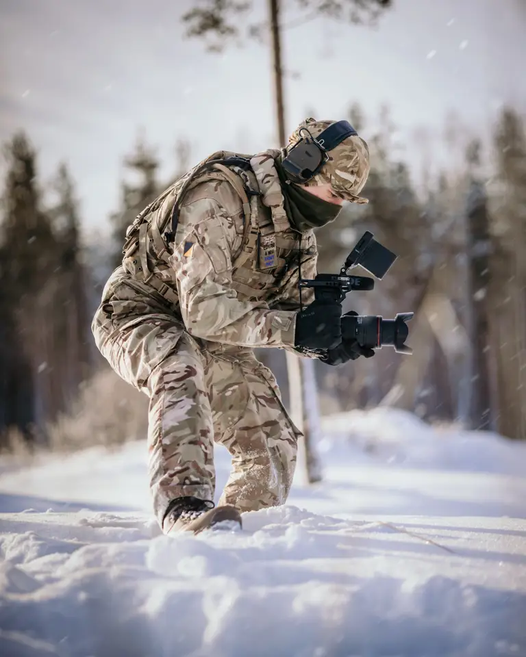 A British Army Photographer holds his camera while he films activity in a snow landscape.