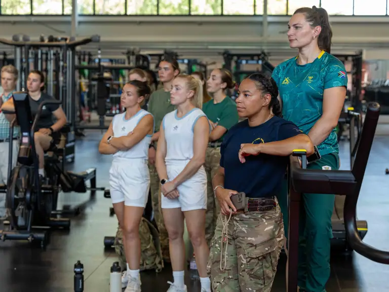 A group of people in athletic attire stand attentively in a gym.