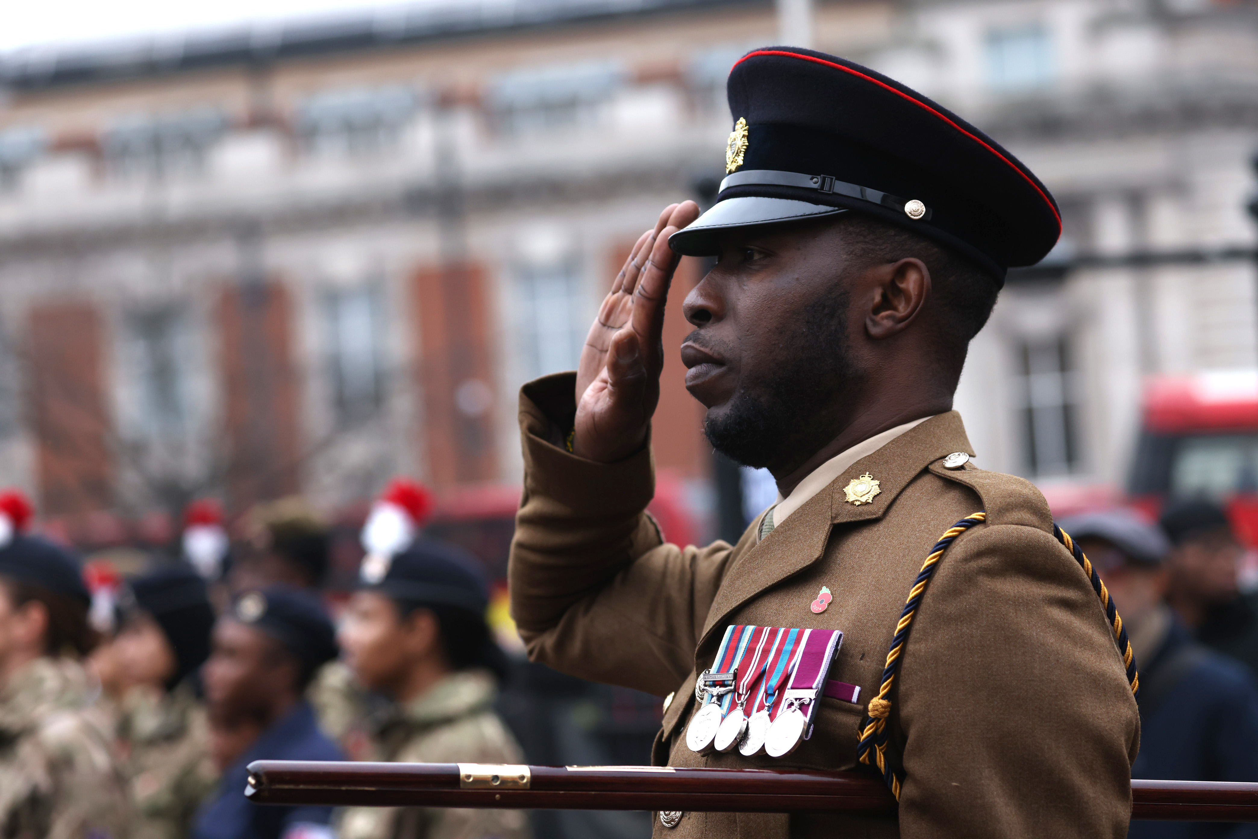 A soldier stands saluting in brown ceremonial uniform.