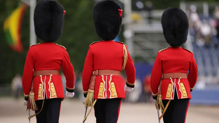 Three soldiers in red tunics and black bearskin hats walk away.