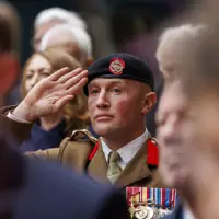 A man in a brown ceremonial uniform and a black beret salutes.
