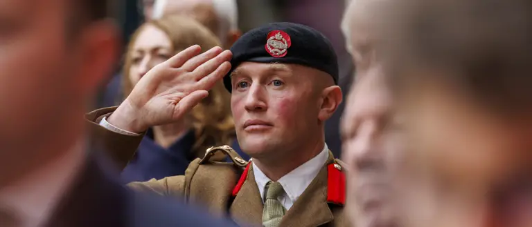 A man in a brown ceremonial uniform and a black beret salutes.