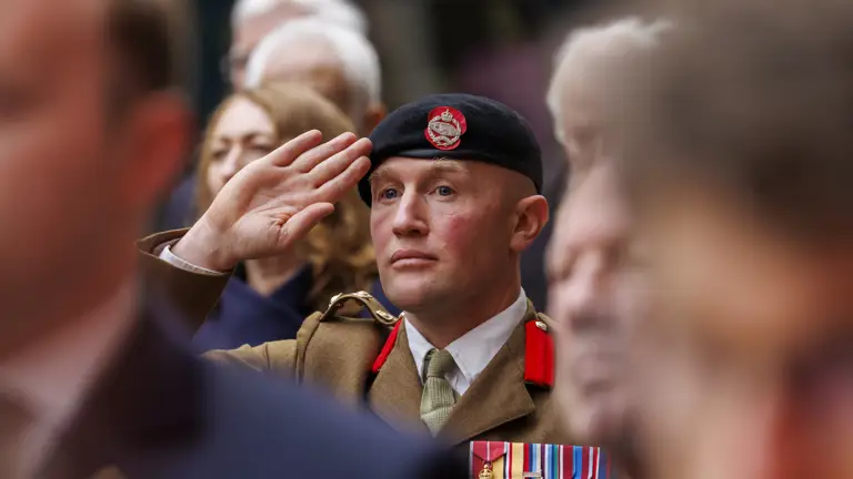 A man in a brown ceremonial uniform and a black beret salutes.