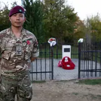 A soldier wearing camouflage uniform and a maroon beret stands in front of a memorial.
