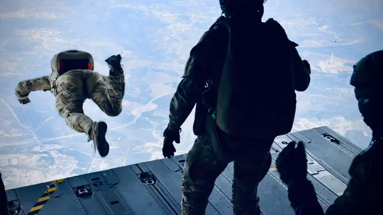 A soldier jumps out the back of a plane while wearing a parachute.