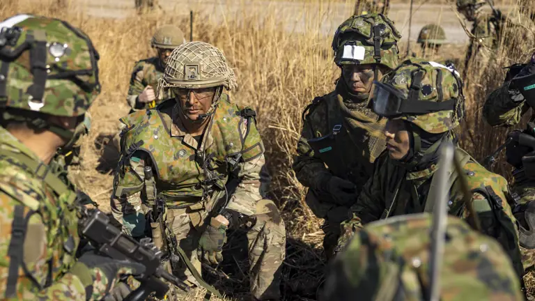 Paratrooper soldier in combat camouflage uniform engaged in planning with the Japanese Ground Self Defence Forces’ soldiers also seen in their combat camouflage uniform on an exercise in a grassy landscape in Japan.