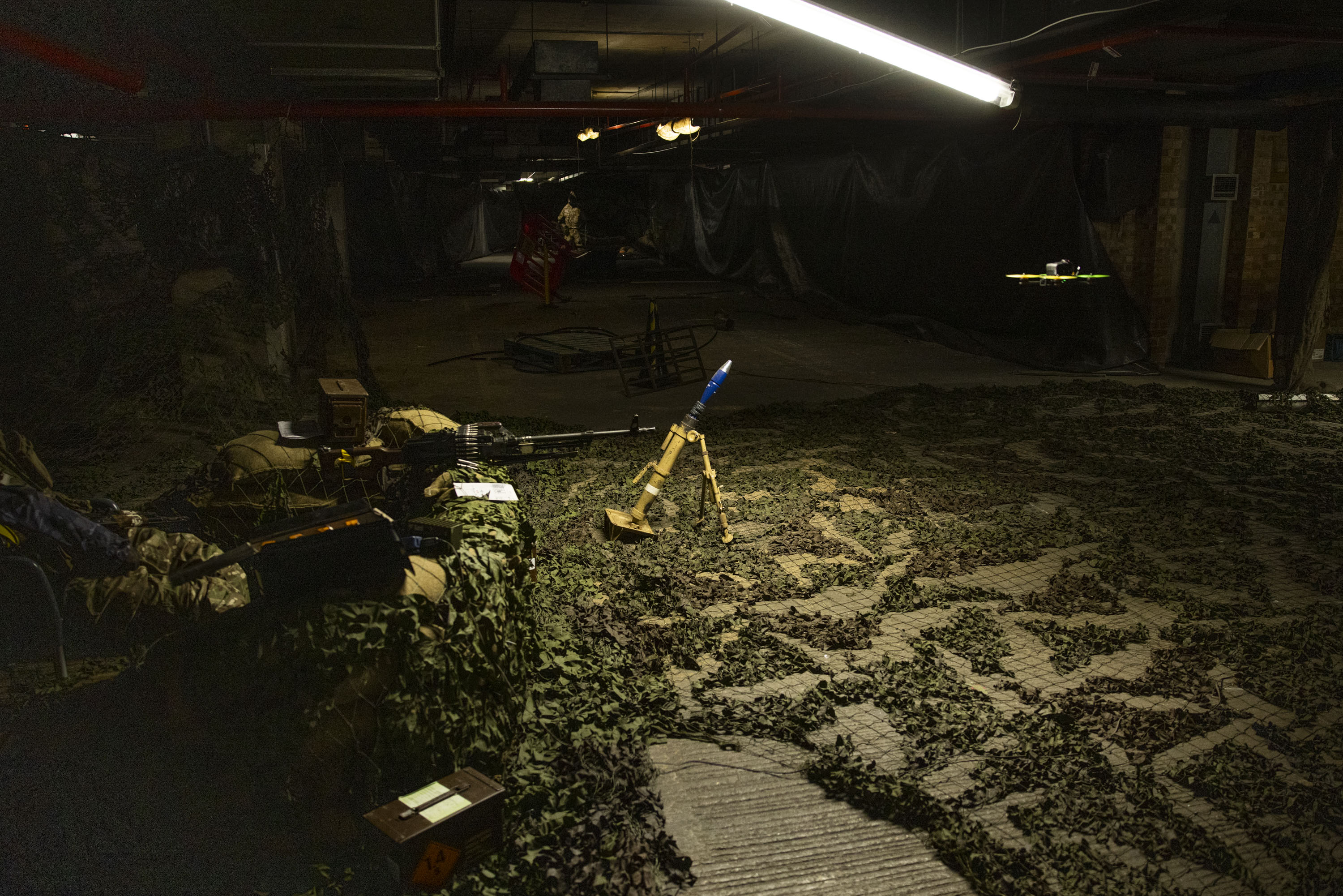 A drone is pictured flying through an artificially created war zone, mortar is located beneath the drone. 