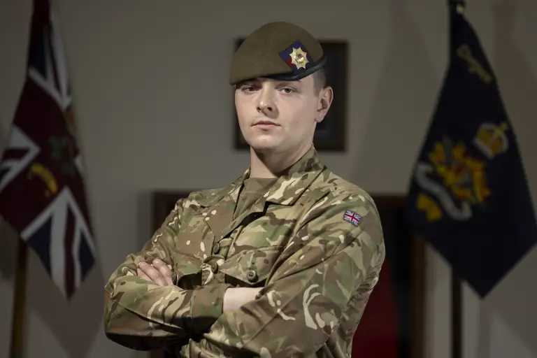 Guardsman stood posing in his camouflage uniform with beret on showing a coldstream guards cap badge.