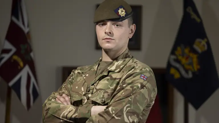 Guardsman stood posing in his camouflage uniform with beret on showing a coldstream guards cap badge.