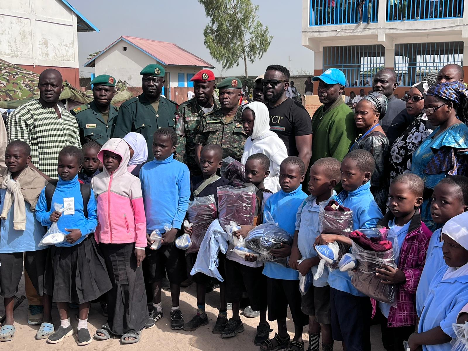 Group of children and uniformed personnel posing outdoors in front of buildings.