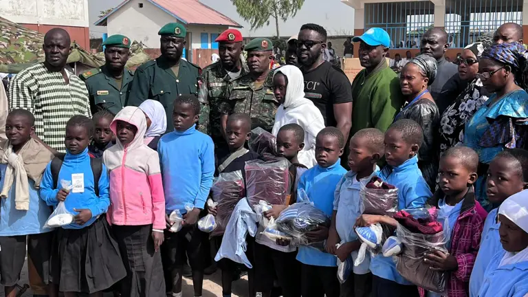 Group of children and uniformed personnel posing outdoors in front of buildings.