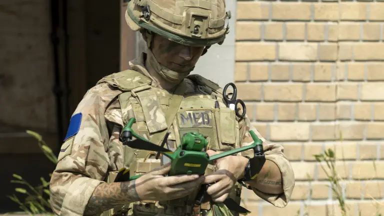 A person in military gear, including a helmet and camouflage uniform labeled with