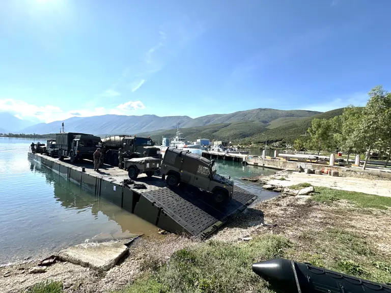 A Land Rover drives off a green military ferry.