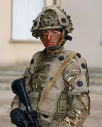 A person in military camouflage gear and helmet stands holding a rifle. Their face is painted with camouflage colours.