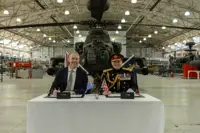 Two men sit in front of a green military helicopter.