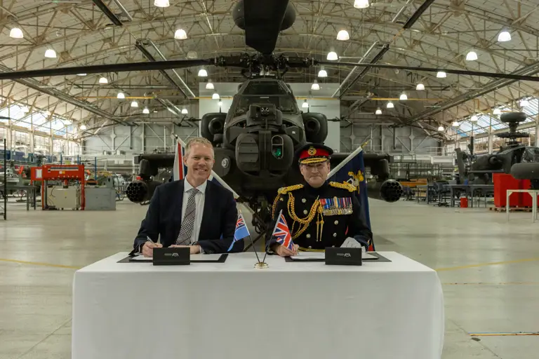 Two men sit in front of a green military helicopter.