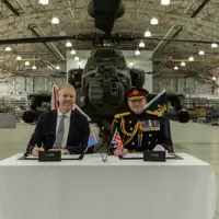 Two men sit in front of a green military helicopter.