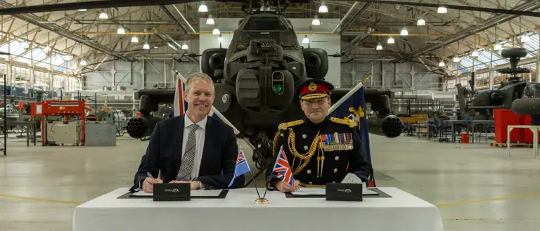 Two men sit in front of a green military helicopter.