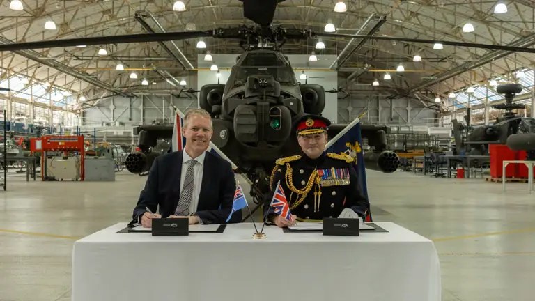 Two men sit in front of a green military helicopter.