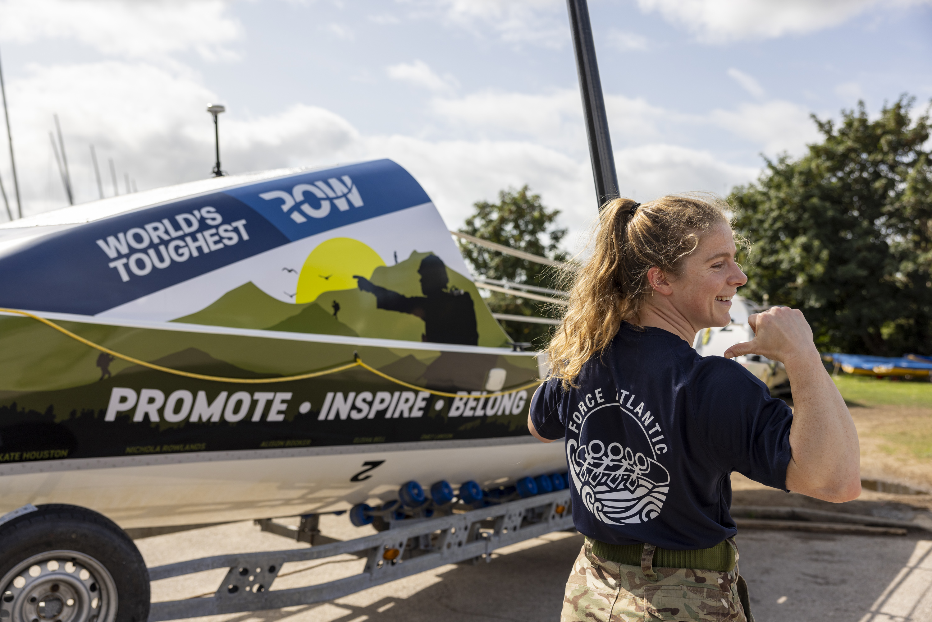 A soldier who is in uniform from the waist down points to the back of her Force Atlantic t-shirt. 