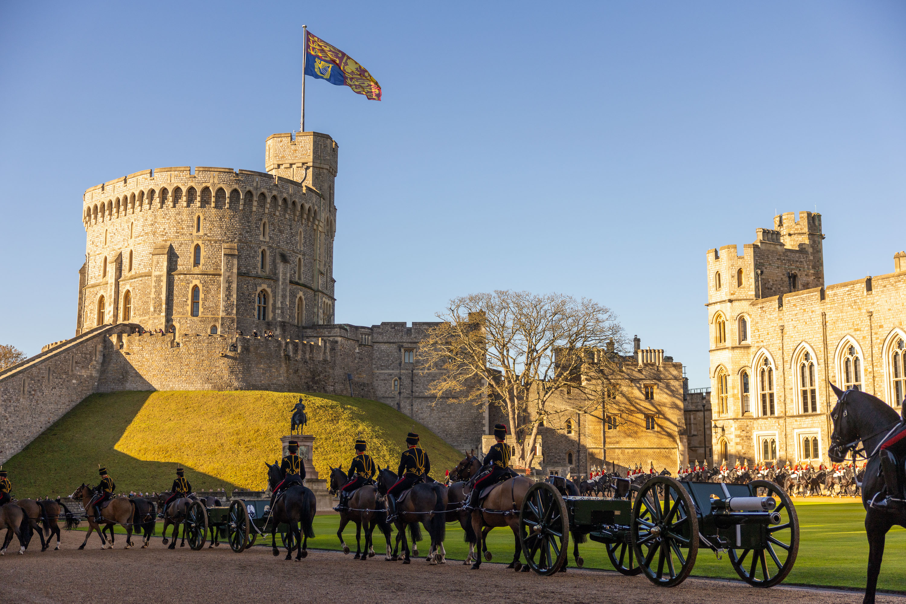 A ceremonial procession with soldiers on horseback and a carriage passes Windsor Castle.