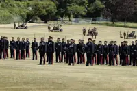A group of soldiers in formal uniforms stands in formation on a grassy field.