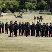 A group of soldiers in formal uniforms stands in formation on a grassy field.