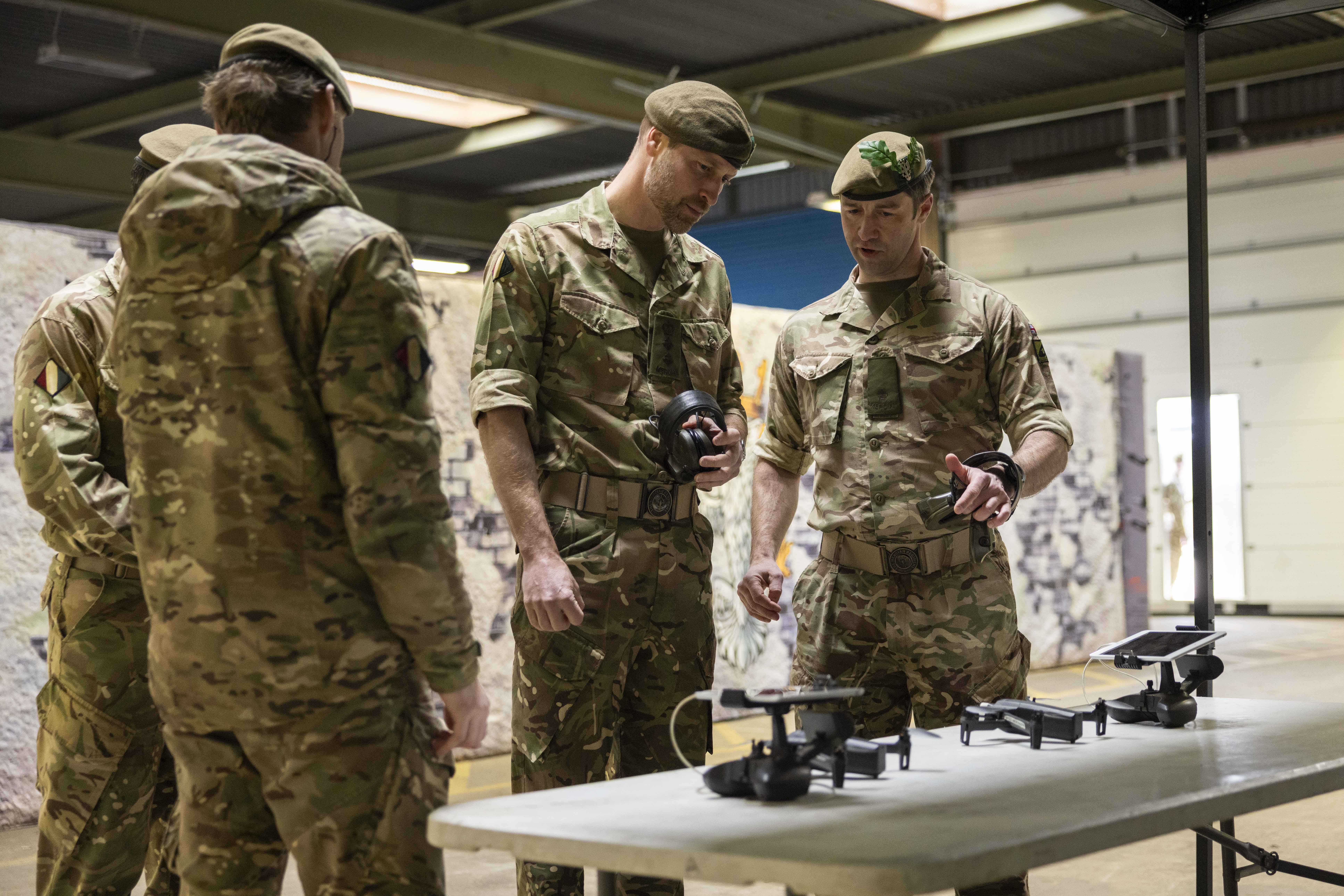 A group of people in military camouflage uniforms are gathered around a table examining drones. 