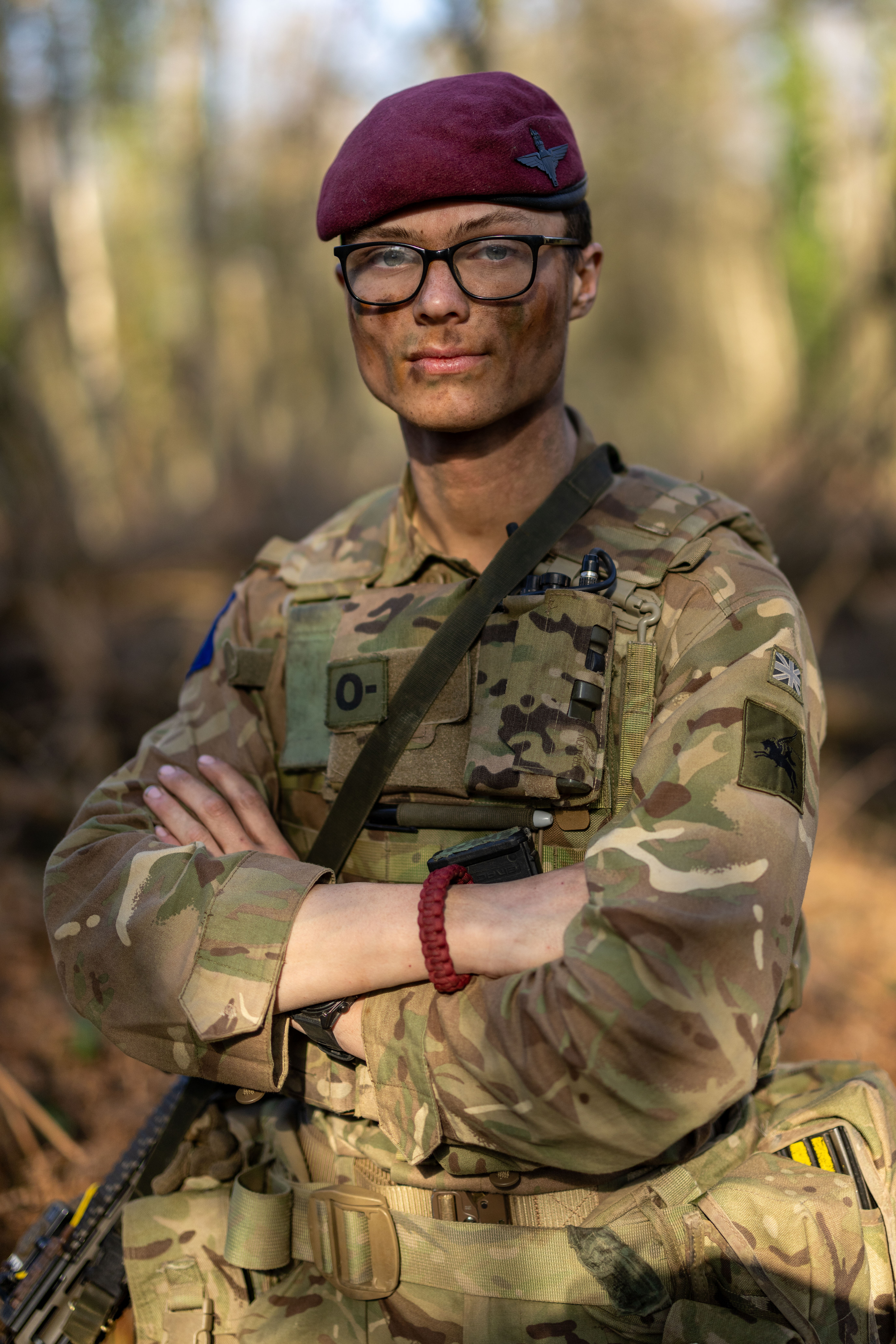 A person in military camouflage uniform and maroon beret, with a patch displaying 