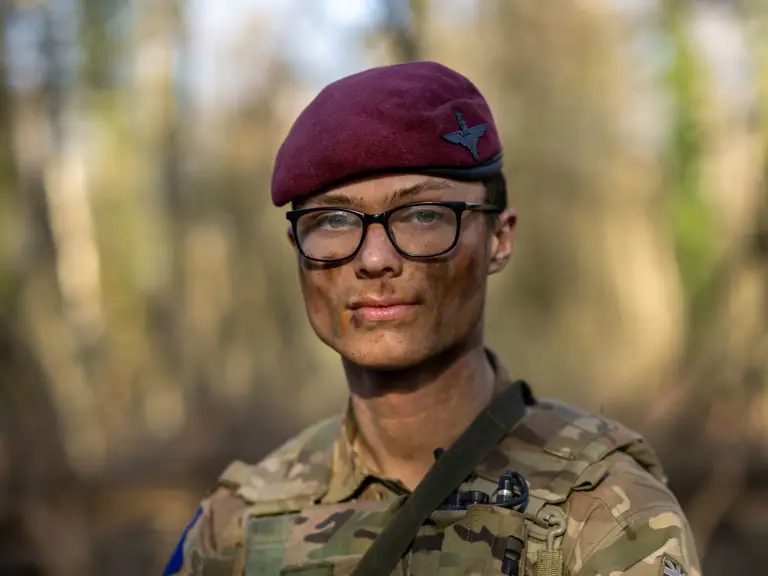 A person in military camouflage uniform and maroon beret, with a patch displaying