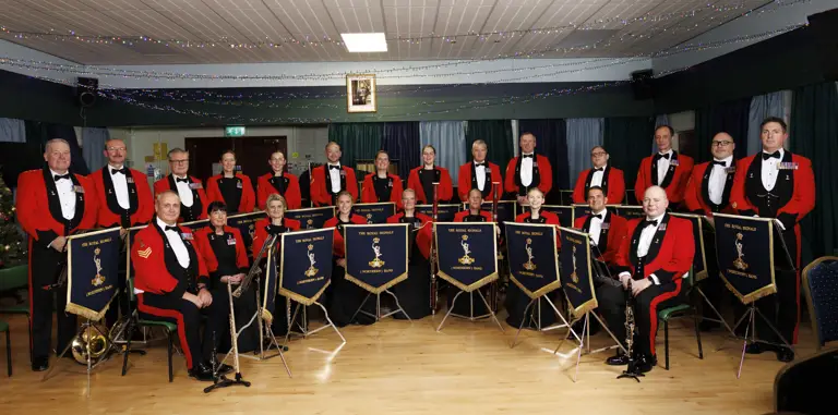 A formal orchestra group dressed in red jackets and black bow ties posing with their instruments.