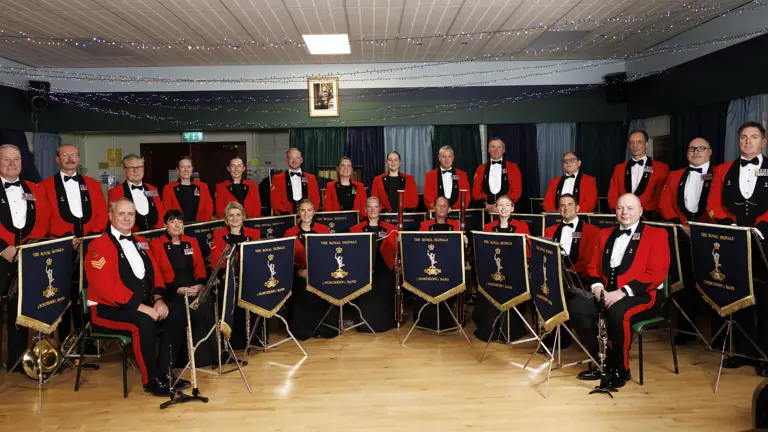 A formal orchestra group dressed in red jackets and black bow ties posing with their instruments.