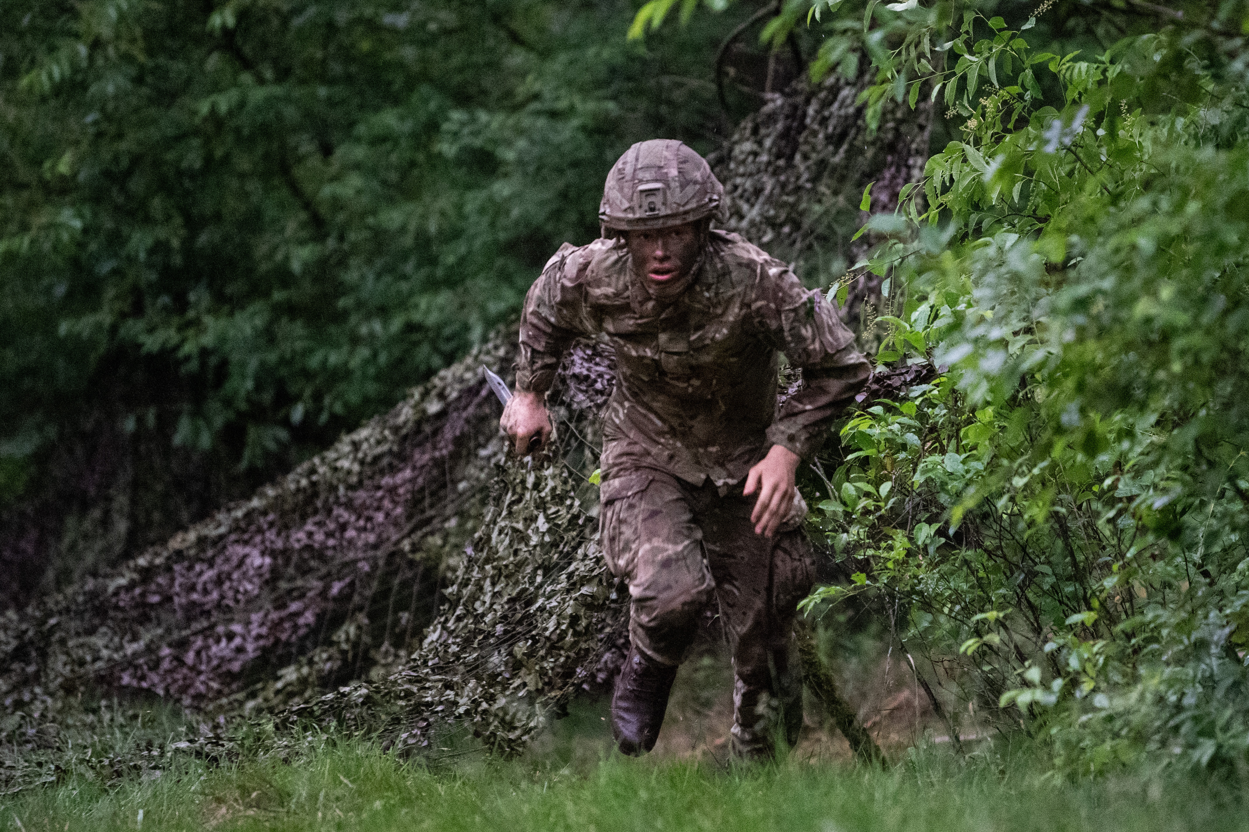 Officer Cadets wearing camouflaged uniform conducting bayonet drills with a Socket Bayonet underneath tree growth.