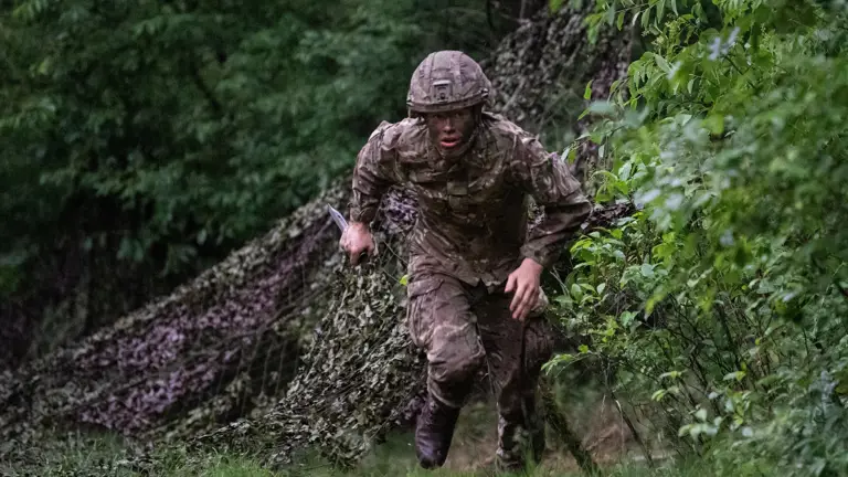 Officer Cadets wearing camouflaged uniform conducting bayonet drills with a Socket Bayonet underneath tree growth.