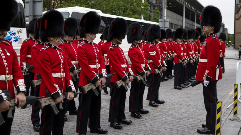 Soldiers in red tunics and black bearskin hats stand on parade outside Kings Cross Station.