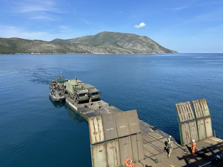 A military ferry carrying green military trucks docks.