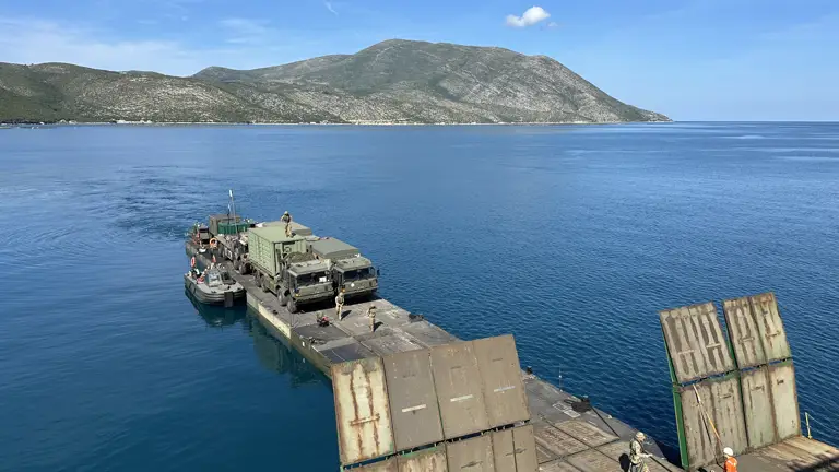 A military ferry carrying green military trucks docks.