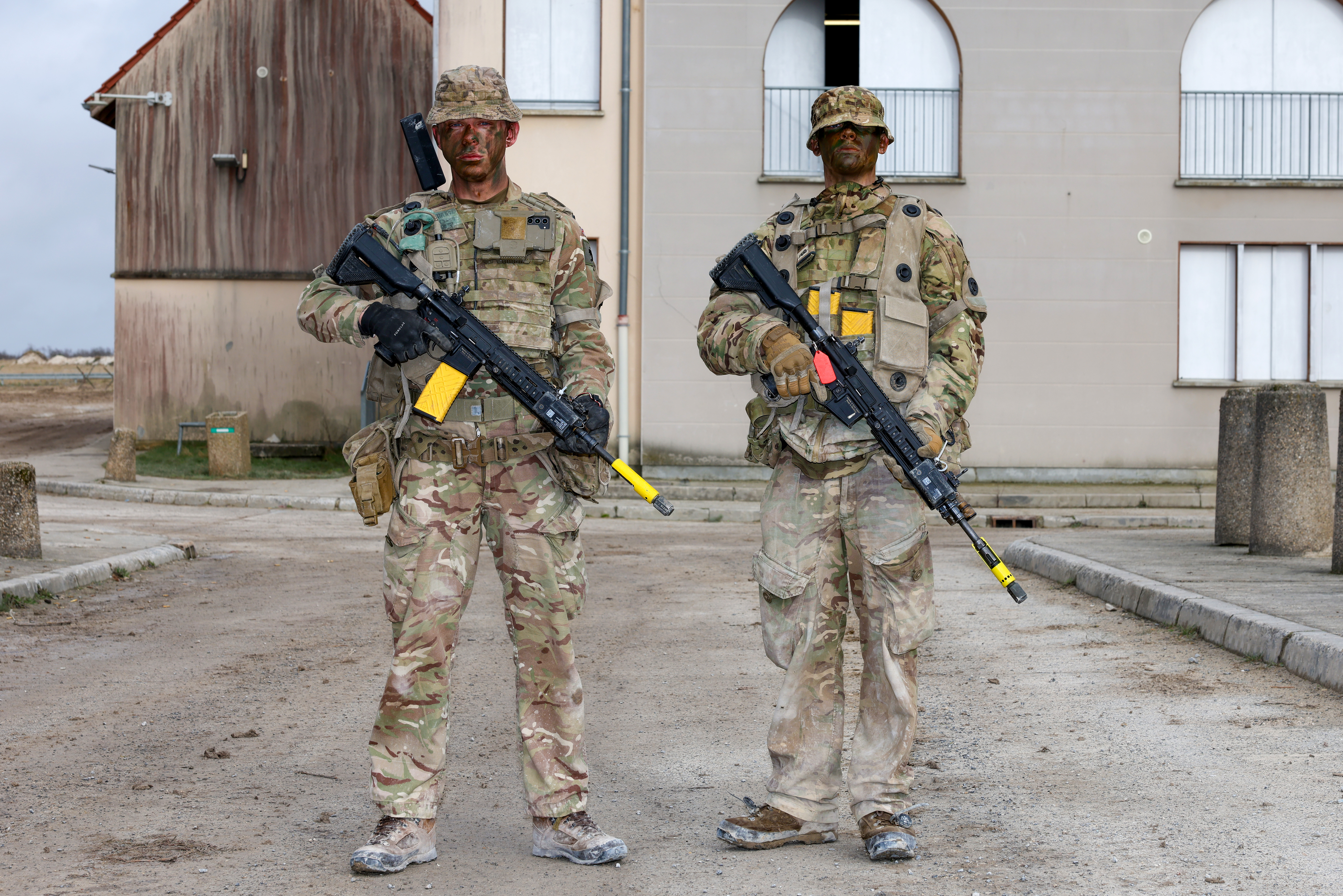 Two soldiers in camouflage uniforms stand next to each other holding rifles. 