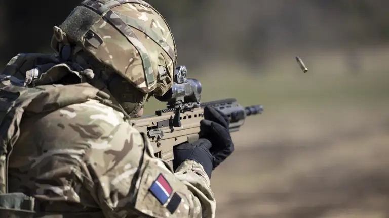 A soldier in British Army uniform is pictured looking down a scope and firing.