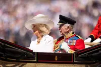 Her Majesty The Queen wearing a white dress and hat sits to the right of His Majesty The King who is wearing British Army ceremonial attire.