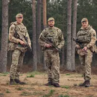 Three brothers stand next to each other wearing camouflage uniforms and holding rifles.