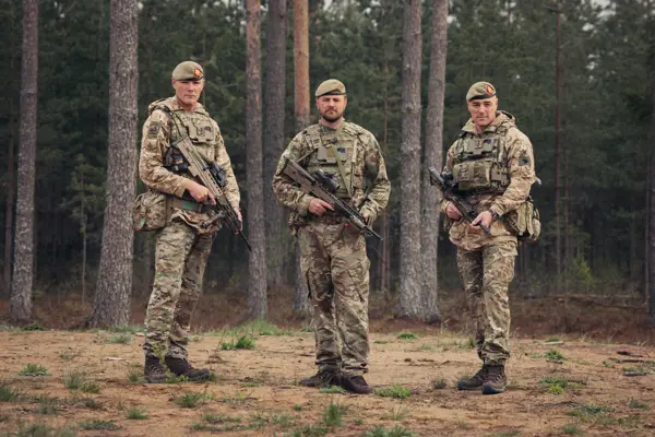 Three brothers stand next to each other wearing camouflage uniforms and holding rifles.