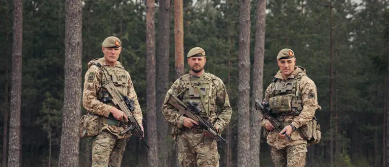 Three brothers stand next to each other wearing camouflage uniforms and holding rifles.