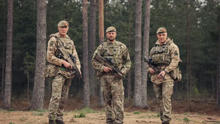 Three brothers stand next to each other wearing camouflage uniforms and holding rifles.