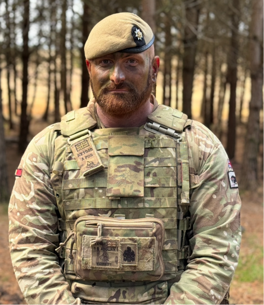 Soldier stood in forest in camouflage with arms clasped in front 
