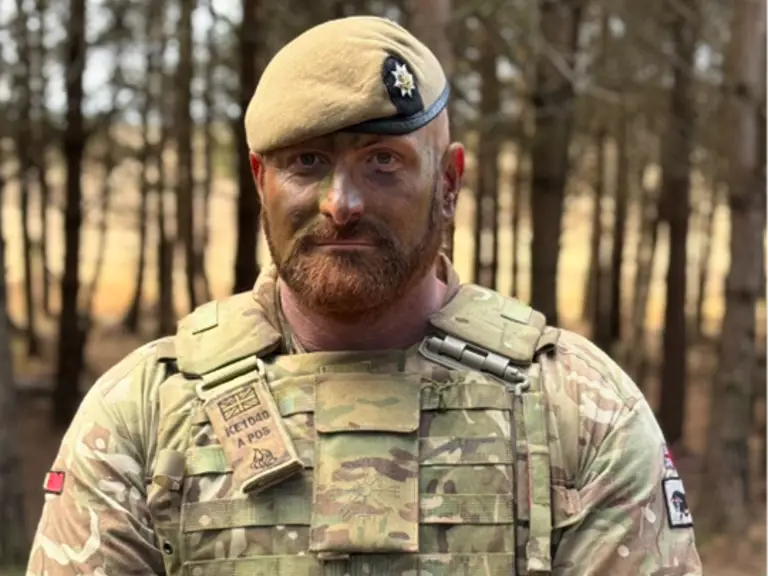 Soldier stood in forest in camouflage with arms clasped in front