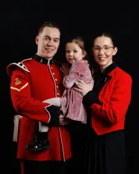 A man in a red military uniform holding a young girl in a pink dress, standing next to a woman wearing the same attire.